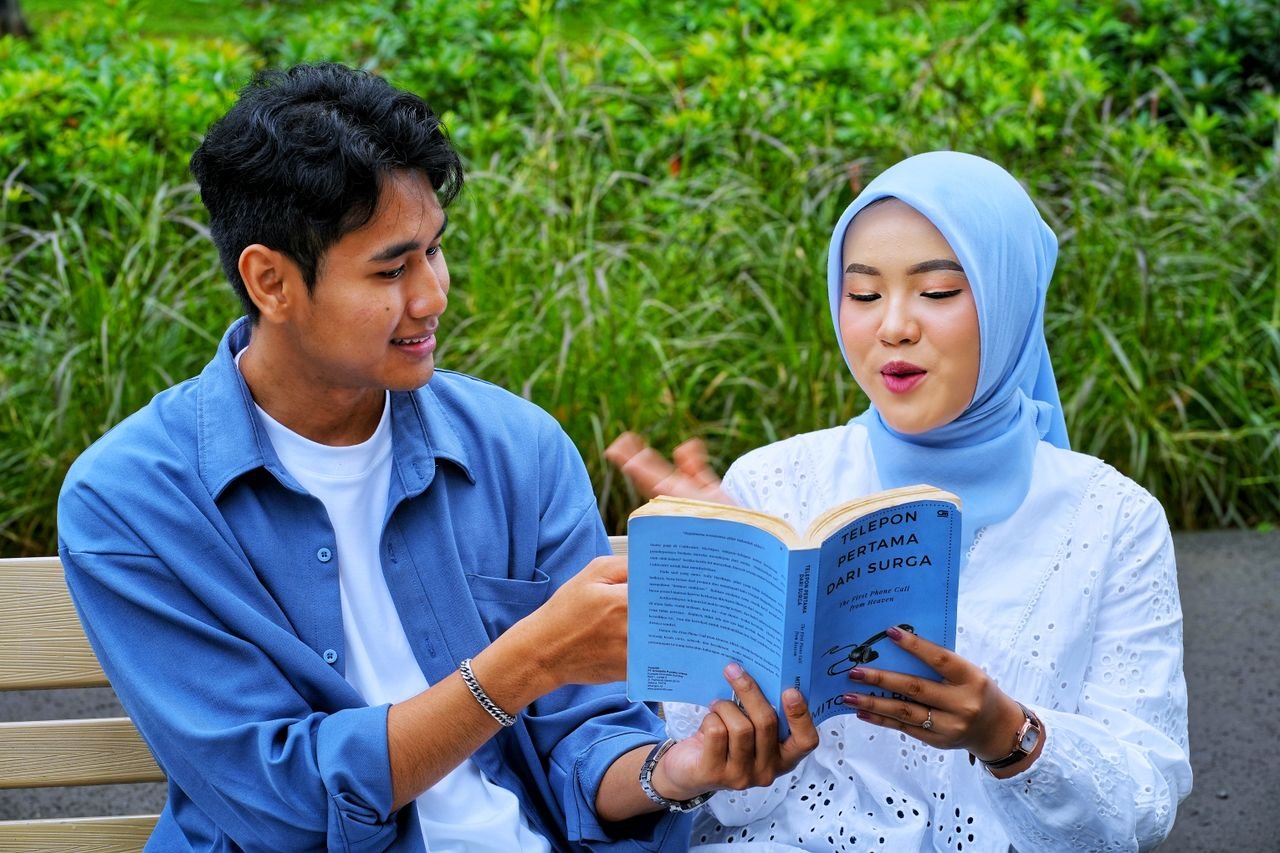 Young couple reading a book together on a park bench, engaging in a leisure activity outdoors.